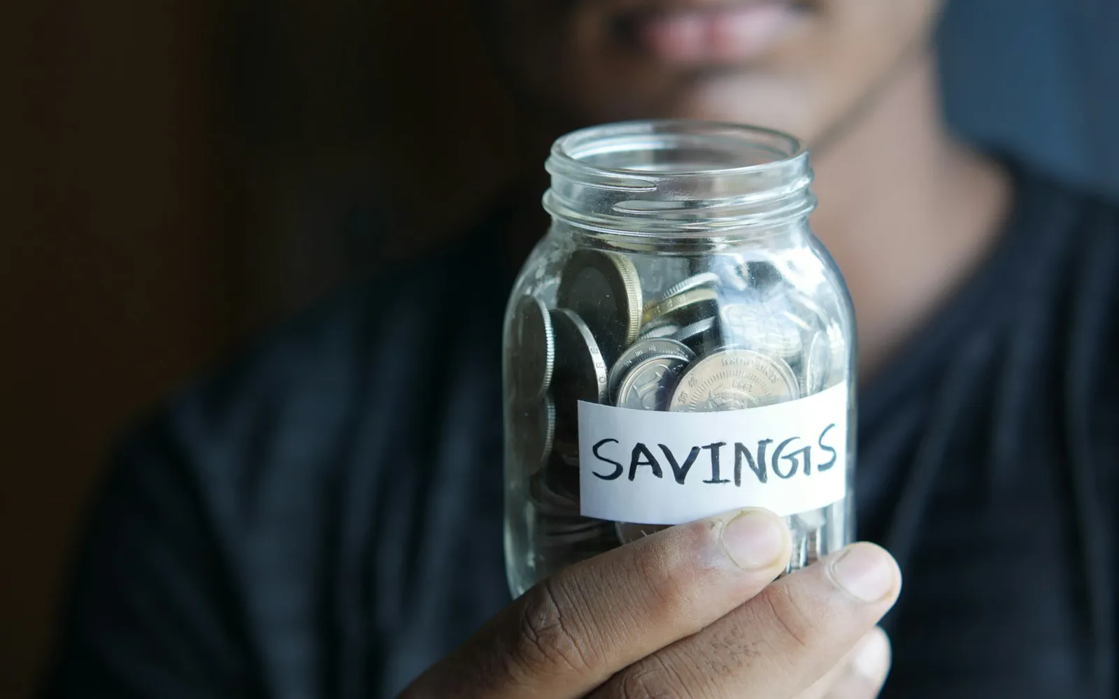 Man holding a glass jar of coins labeled savings