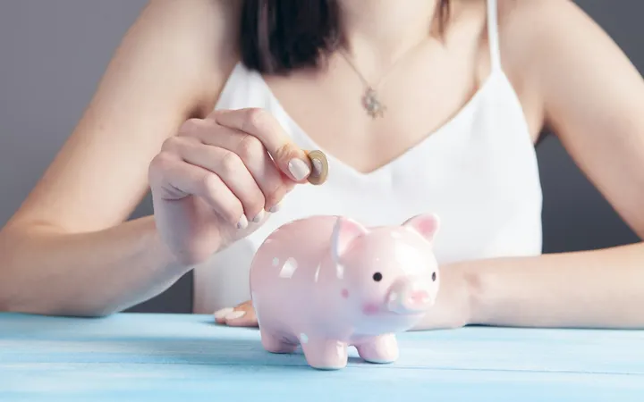 Woman dropping a coin into a pink piggy bank
