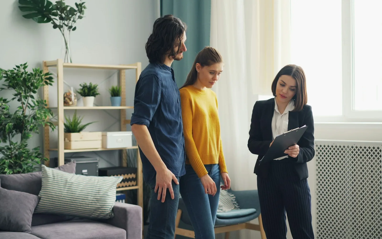 Home inspector with a clipboard talking to buyers in a living room
