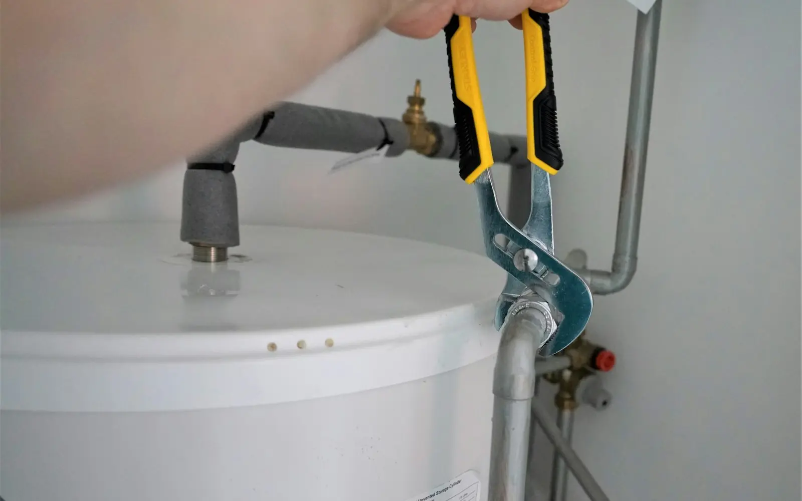 A plumber tightening a pipe fitting on top of a white tank water heater